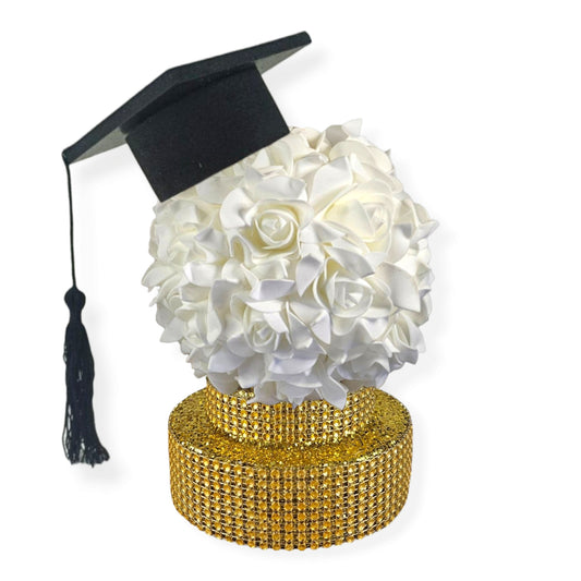 Graduation centerpiece with black cap, white rose kissing ball, and gold glitter base with rhinestone ribbon.